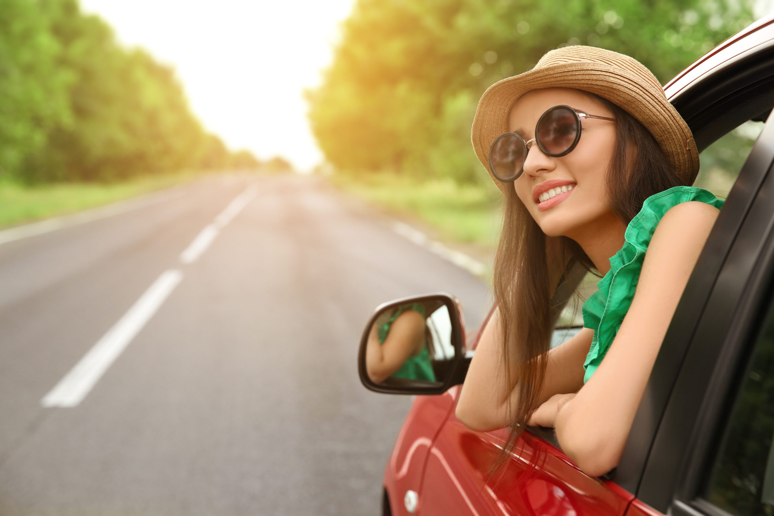 A woman sticking her head out of a moving car as it drives down a road.